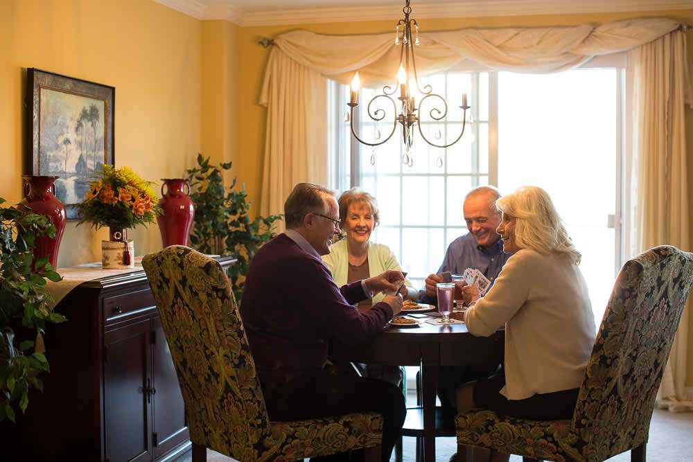 A group of seniors playing cards around a dining table in a well-lit room.