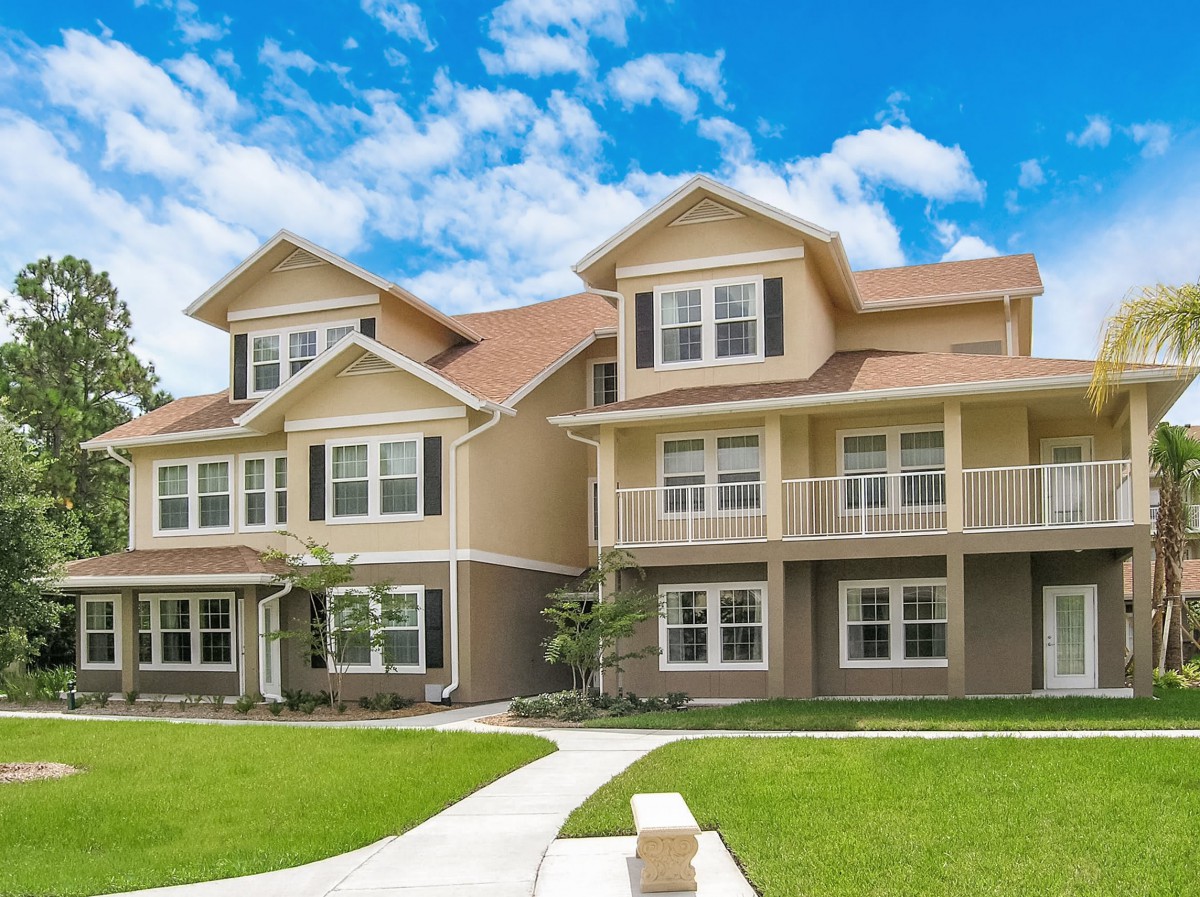 A charming two-story duplex in a suburban neighborhood with a well-maintained lawn and clear blue sky.