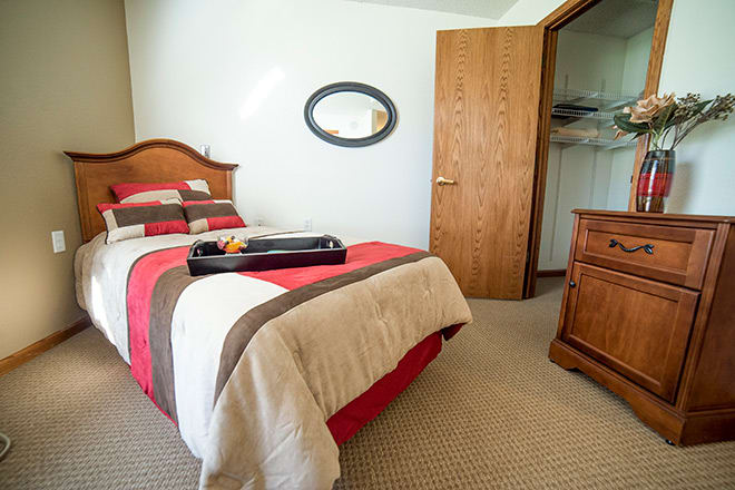 A cozy bedroom features a single bed with a striped duvet, wooden furniture, and an open closet door.