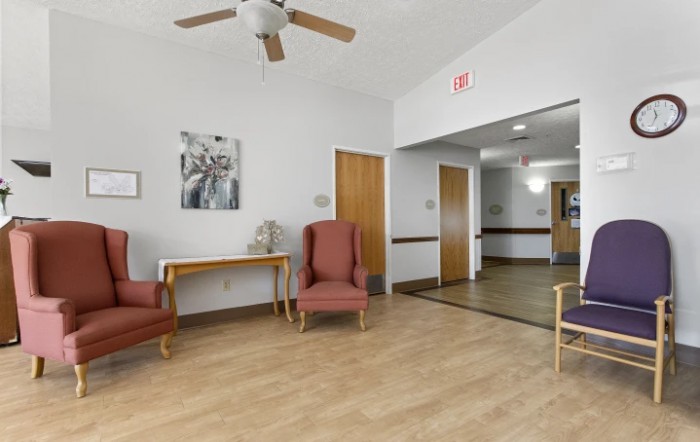 A cozy waiting area with wooden flooring, armchairs, a ceiling fan, and decorative elements.