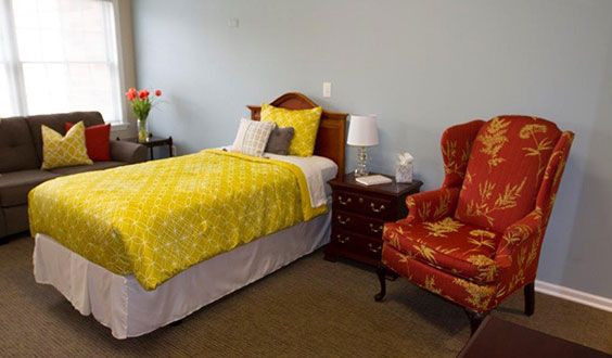Single bedroom with a yellow bedspread, red armchair, and wooden nightstand.