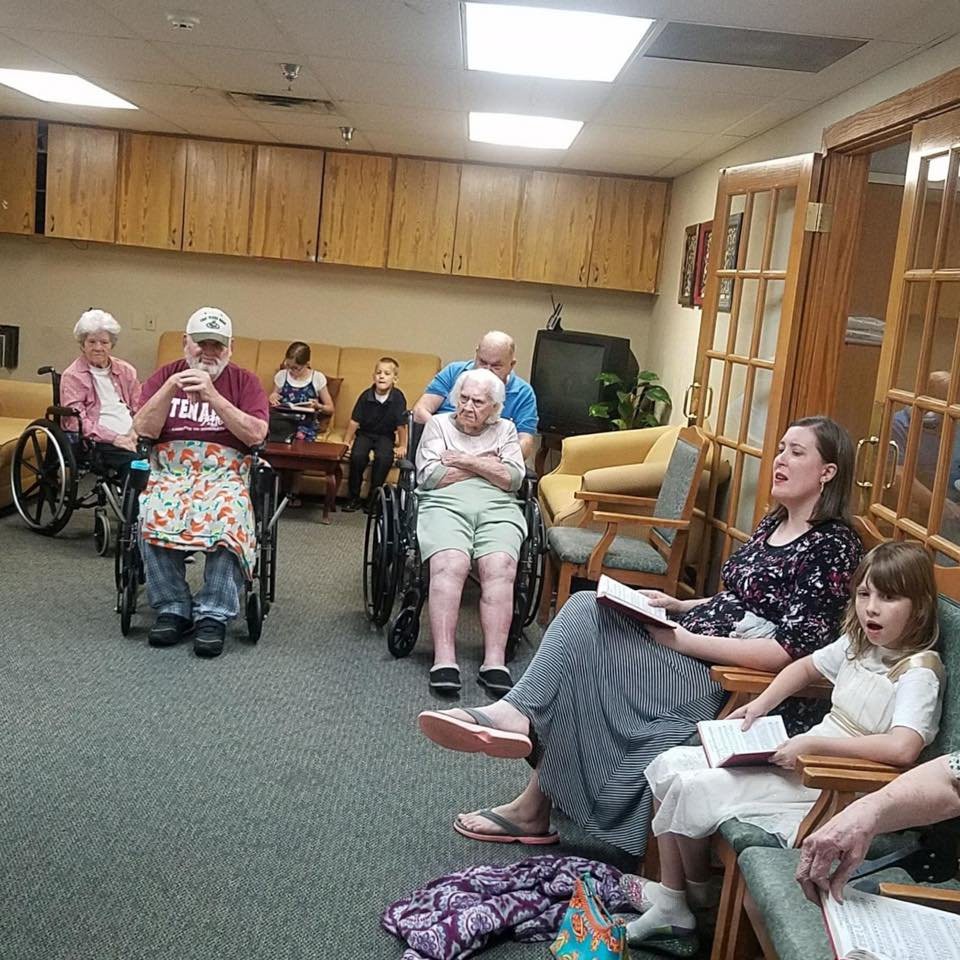 A group of elderly individuals and a young girl participate in a community gathering at a nursing home.