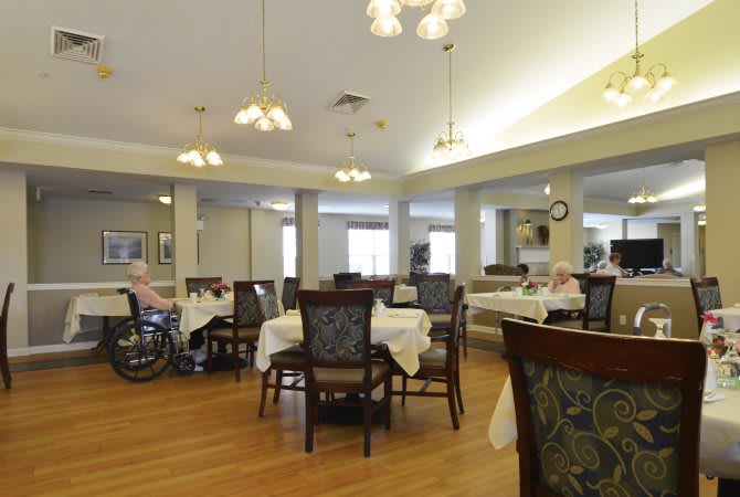 A well-lit dining area with multiple tables and chairs, featuring a wooden floor and decorated with hanging lights.