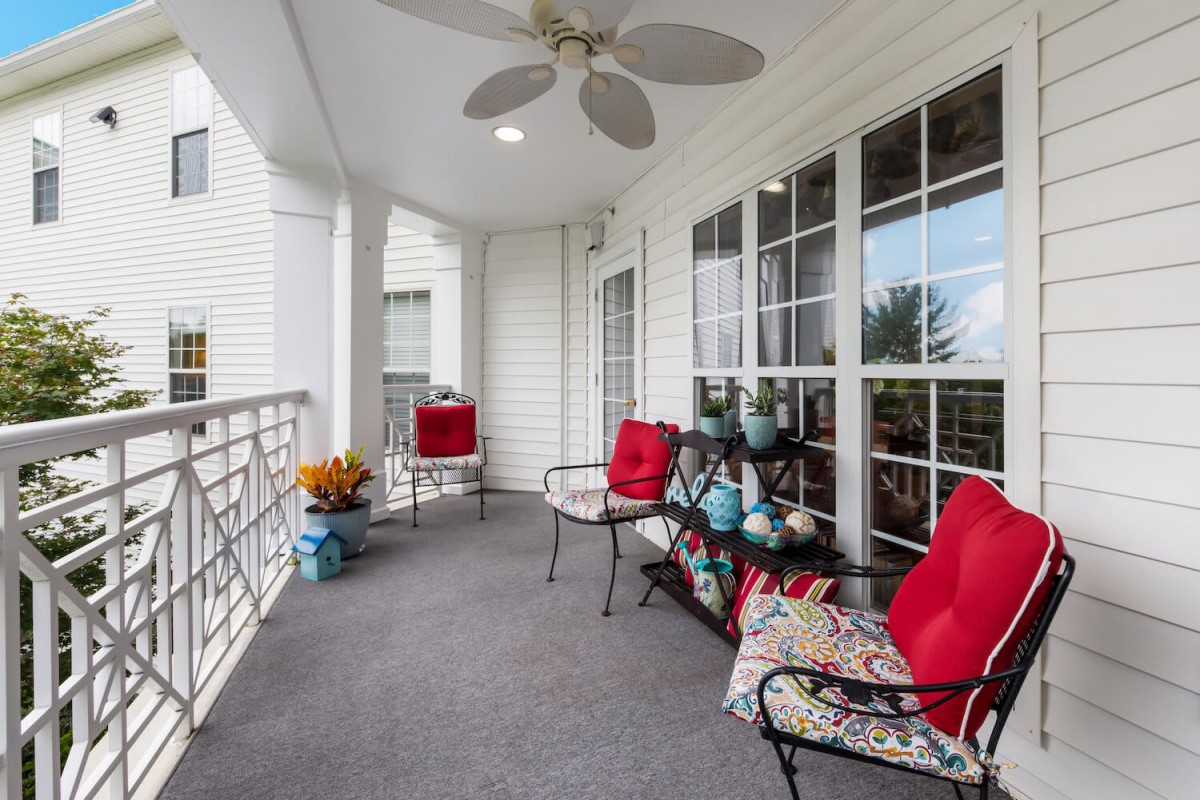 A cozy balcony with red-cushioned patio furniture and a ceiling fan, perfect for relaxing outdoors.