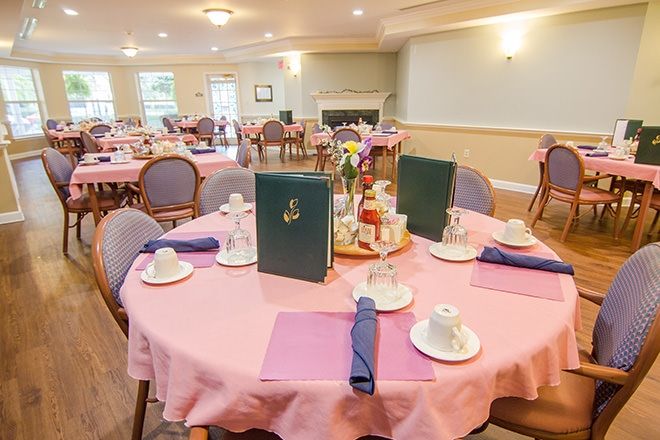 A well-arranged dining room with tables set for service, featuring pink tablecloths, neatly folded napkins, and decorative centerpieces.