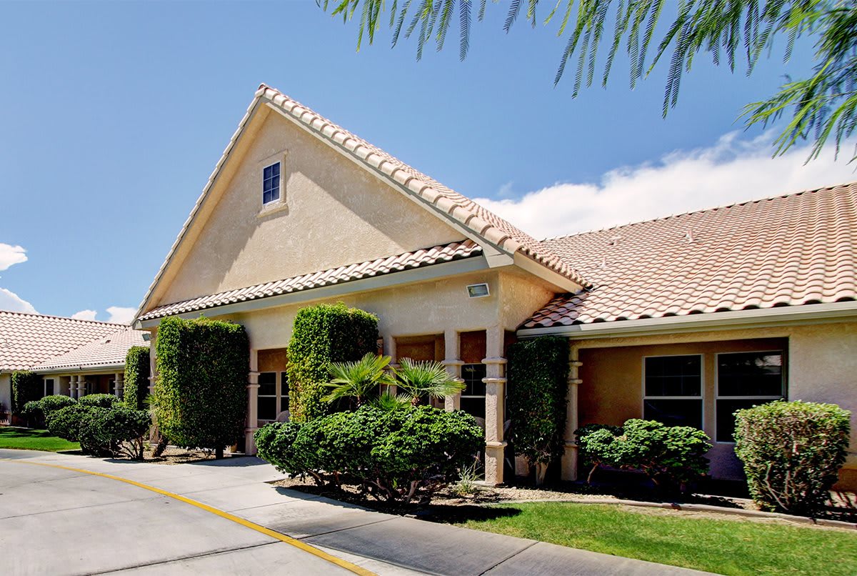 A sunny exterior view of a house with a sloped roof, surrounded by lush greenery.