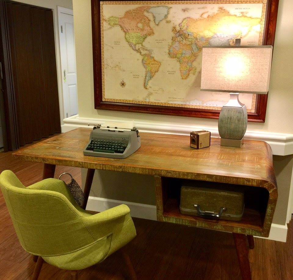 A vintage home office setup with a typewriter, map on the wall, and a cozy lamp.