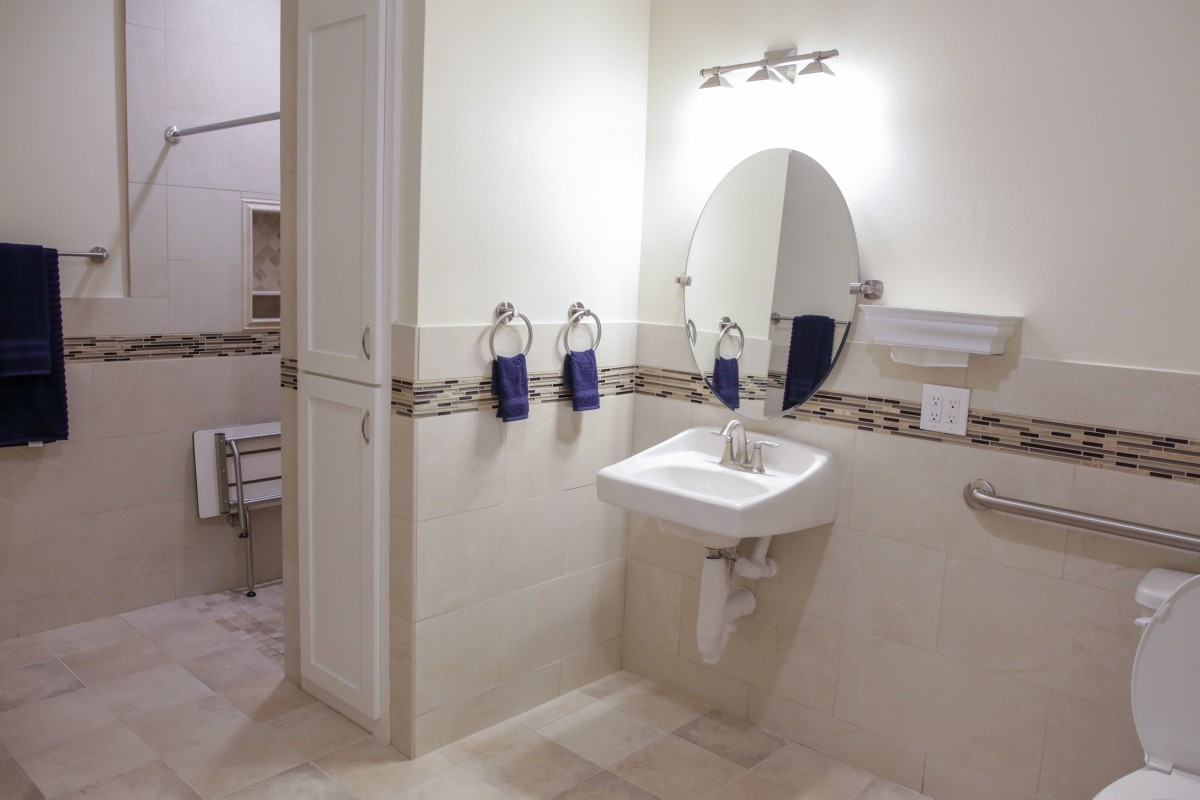 A modern bathroom with a wall-mounted sink, oval mirror, and purple towels.
