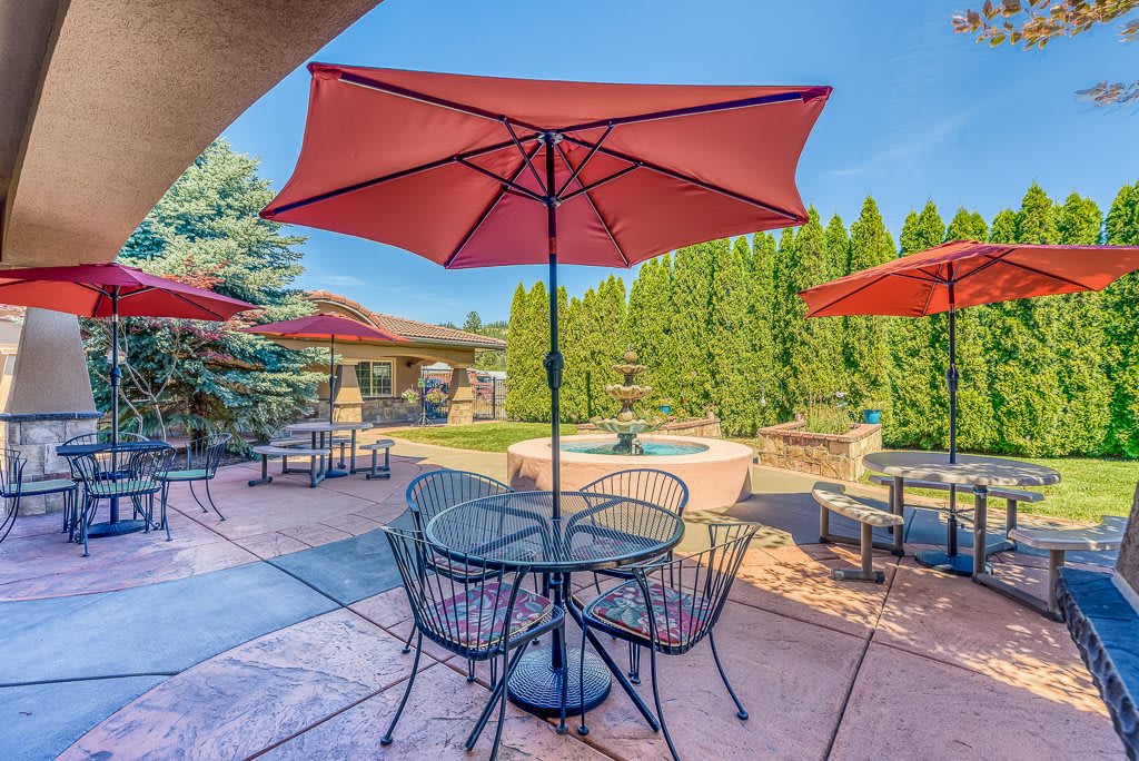 A sunny patio with tables, chairs, and red umbrellas.