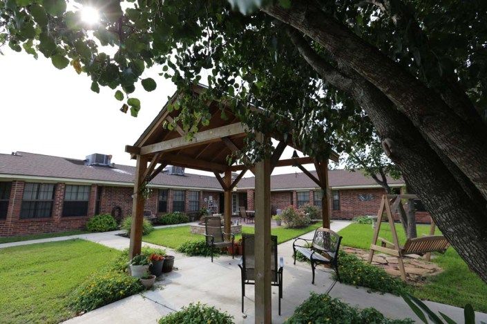 A serene outdoor courtyard featuring a wooden gazebo surrounded by lush greenery and seating.