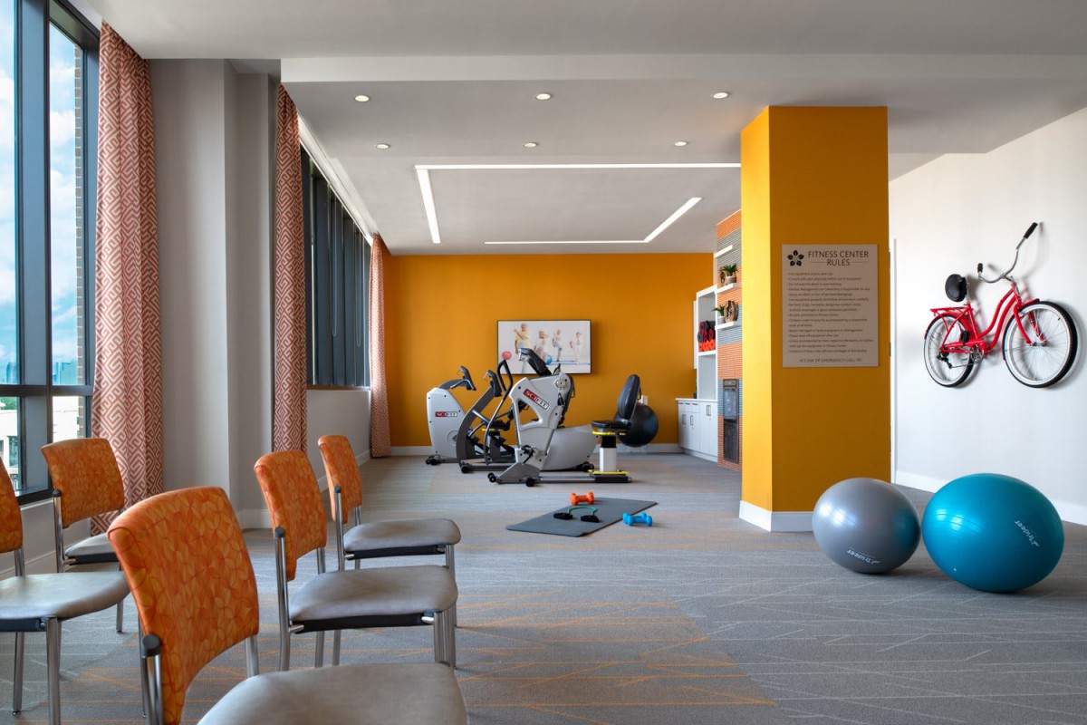 A modern gym interior with exercise equipment and vibrant orange accents.