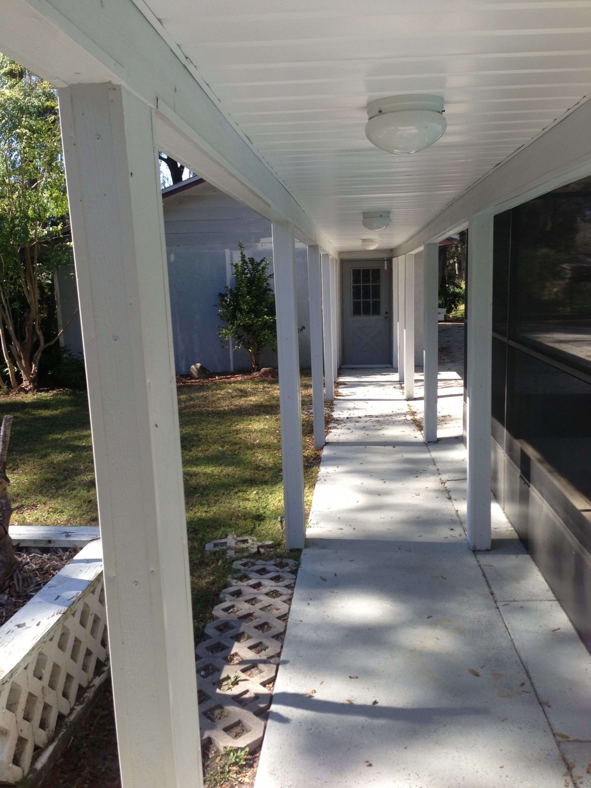 A covered outdoor walkway with white columns and a concrete path leading to the backyard.