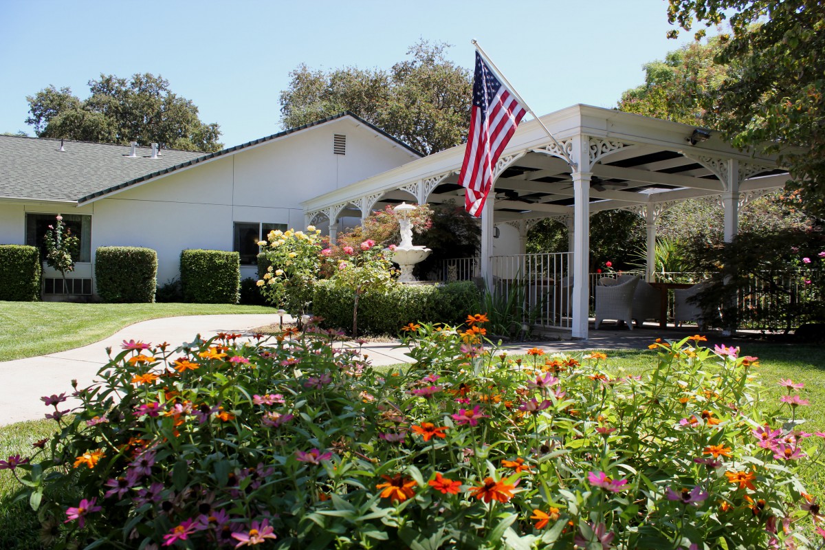 A charming house with a beautifully landscaped garden featuring colorful flowers, a fountain, and an American flag on display.