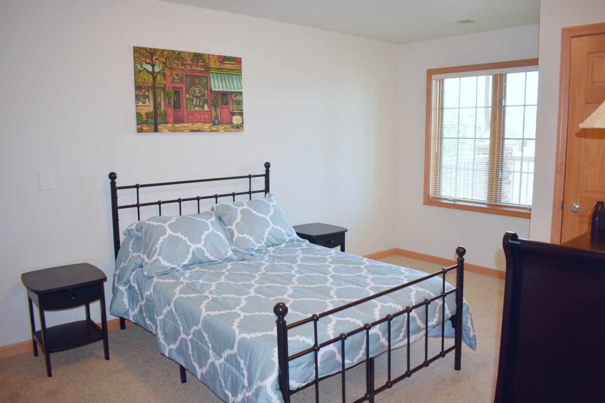 A tidy bedroom featuring a metal bed frame with patterned bedding, a painting on the wall, and a window bringing in natural light.