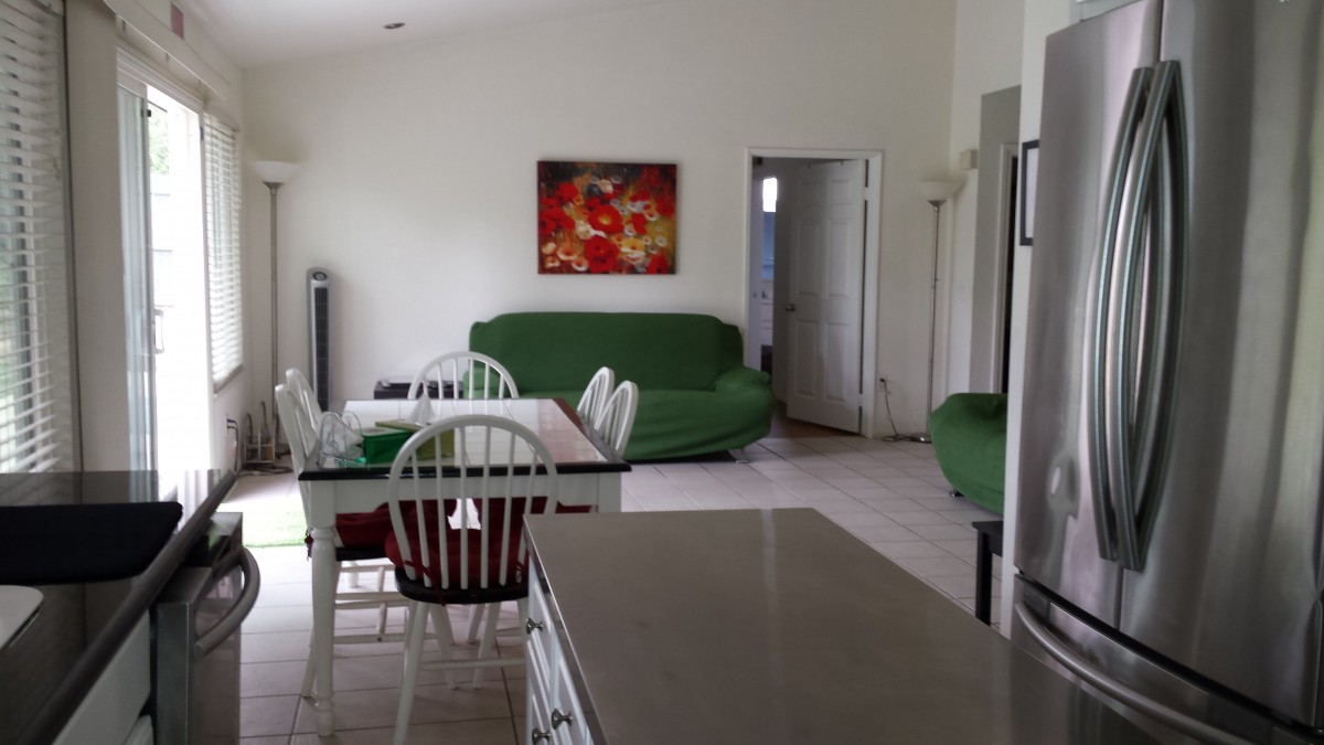 A cozy living room with a dining area featuring green sofas, a dining table with chairs, and wall art.