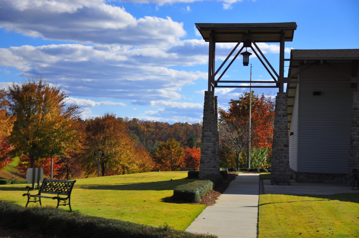 A scenic view of a bell tower with autumn foliage and a bench under a partly cloudy sky.