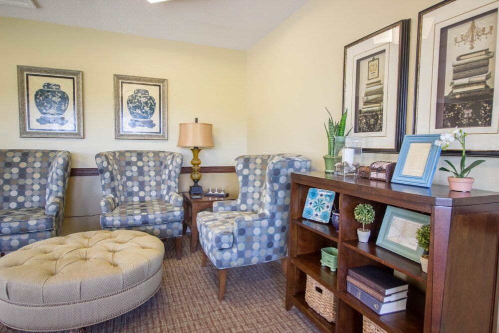 A cozy living room with patterned chairs, an ottoman, and a bookshelf filled with books and decor.