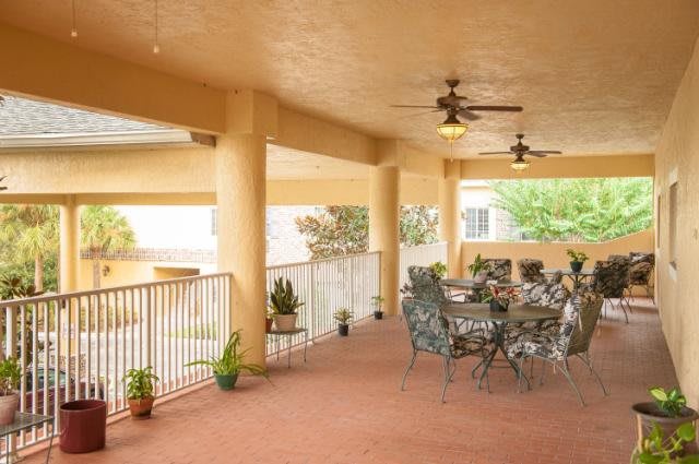 A spacious covered patio with ceiling fans, featuring a table and chairs surrounded by potted plants.