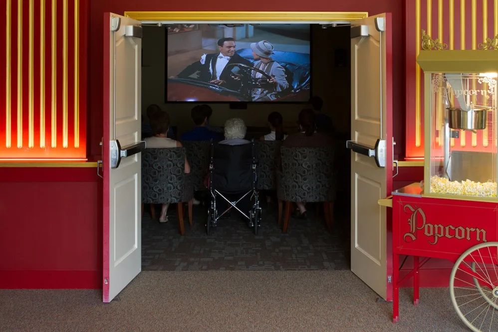 A group of people watching a movie in a small screening room, with one person in a wheelchair.