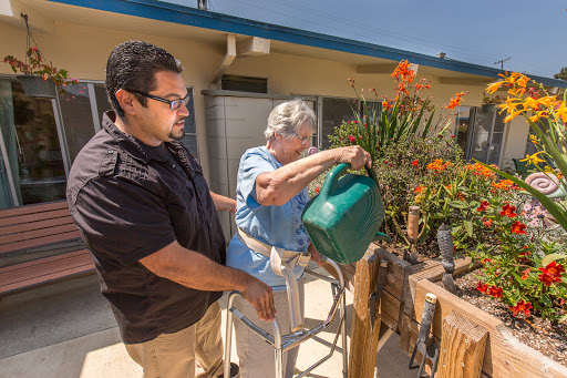 A caregiver assists an elderly woman as she waters plants, showcasing the beauty of community support and gardening.