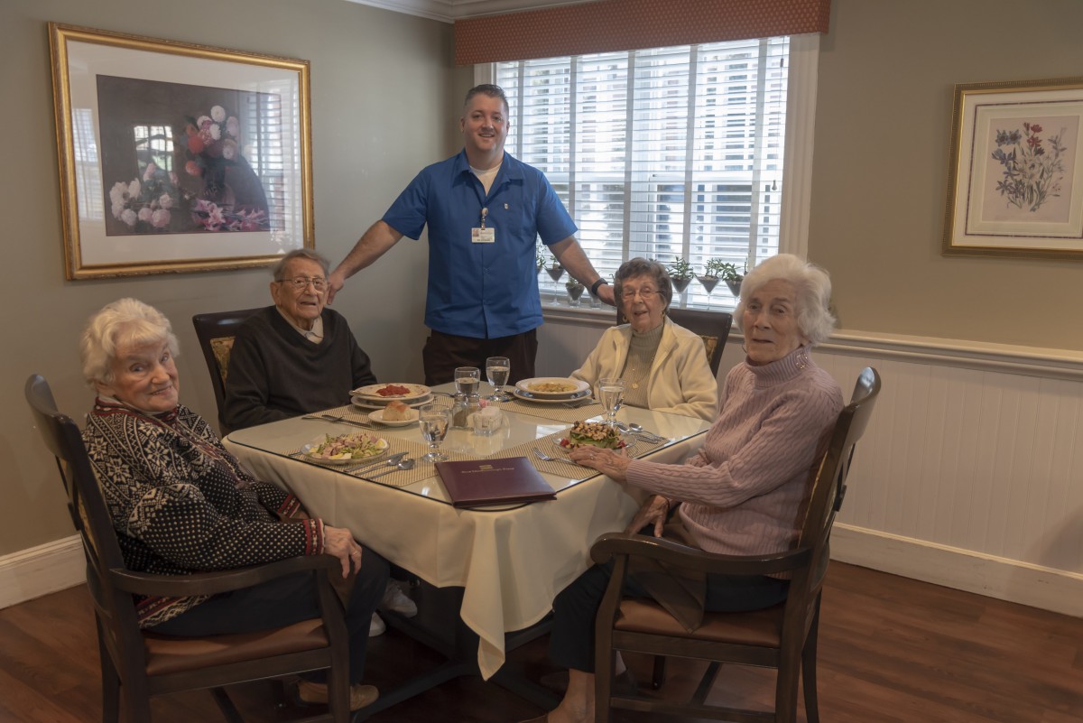Elderly individuals dining together with a caregiver in a cozy setting.