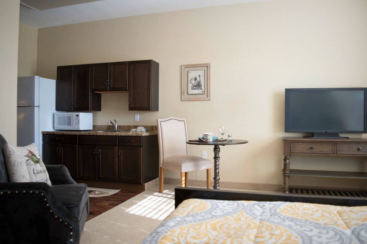 A cozy hotel room featuring a kitchenette, small dining area, and a television.