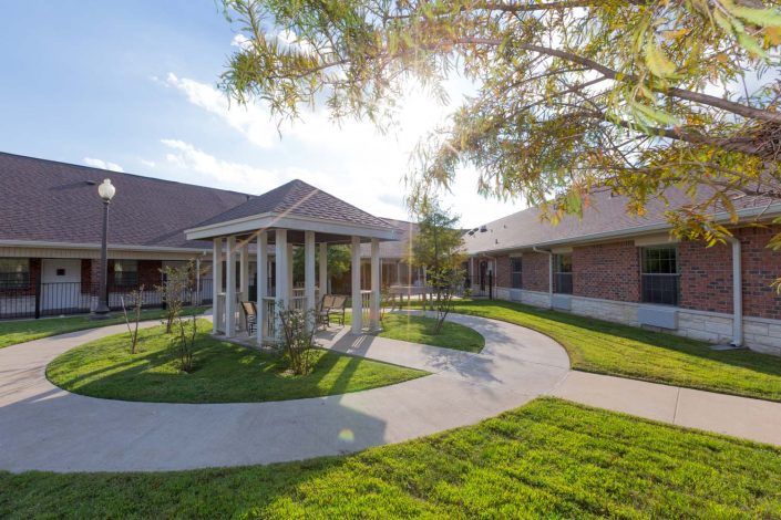A sunny courtyard with a curved pathway and well-maintained landscaping surrounded by buildings.