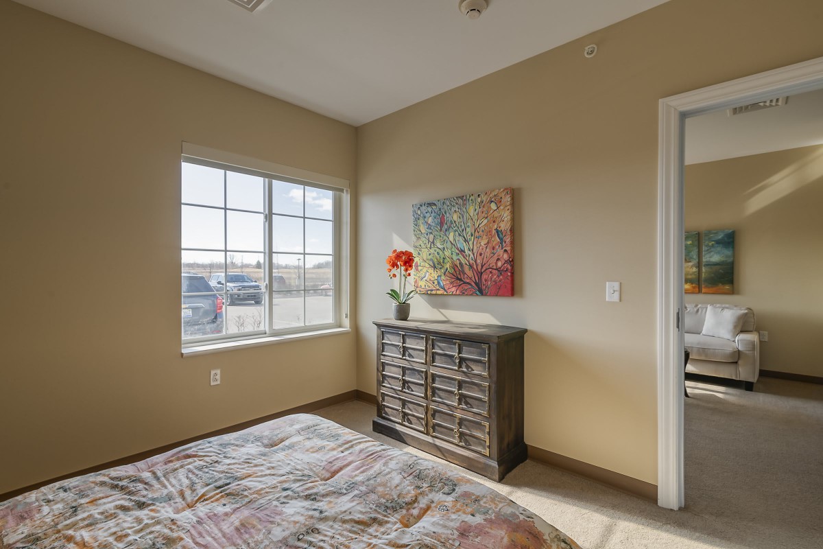 A cozy bedroom with a window, dresser, and colorful decor.