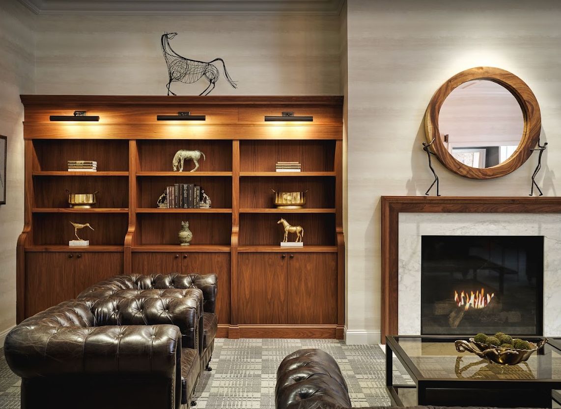 A cozy library lounge with leather seating, bookshelves, and a fireplace.