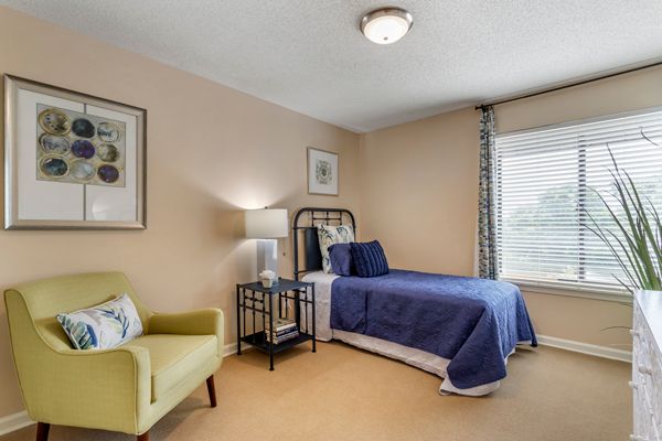 A cozy bedroom featuring a single bed with blue bedding, an armchair, and decorative wall art.