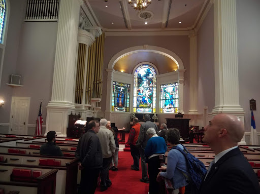 A gathering of people inside a church, showcasing beautiful stained glass windows and classic architectural elements.