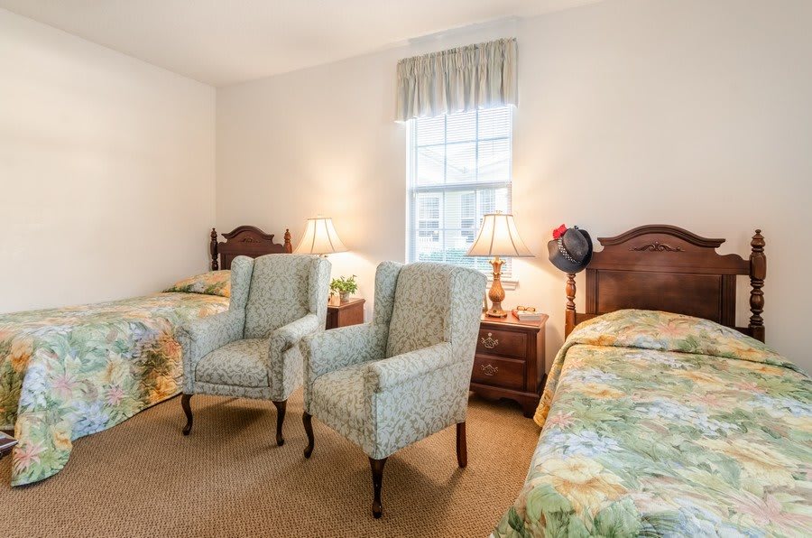 A cozy bedroom featuring two beds, two upholstered chairs, and a window with a curtain.