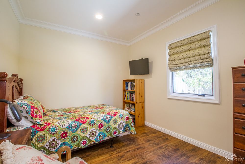 A cozy bedroom featuring a single bed with a colorful bedspread, a small bookshelf, and a wall-mounted television.