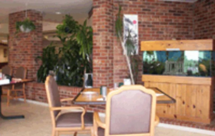 A cozy interior space featuring a table and chairs, with a brick wall, lush plants, and an aquarium.