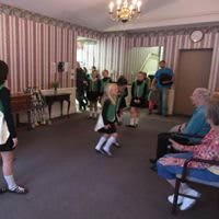 Children performing a dance for an audience of seniors in a living room setting.