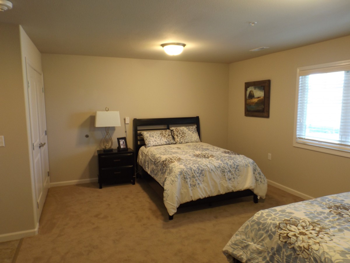 A cozy bedroom with a double bed, nightstand, and lamp, featuring neutral decor and carpet flooring.