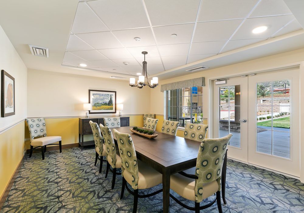 A well-lit dining or conference room with a long wooden table surrounded by chairs and adorned with a chandelier and decorative wall art.