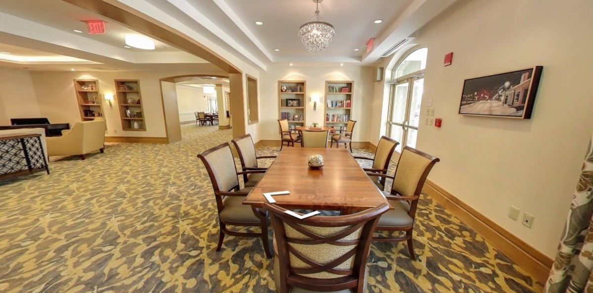 A modern conference room featuring a long table, surrounded by chairs, and flanked by bookshelves.