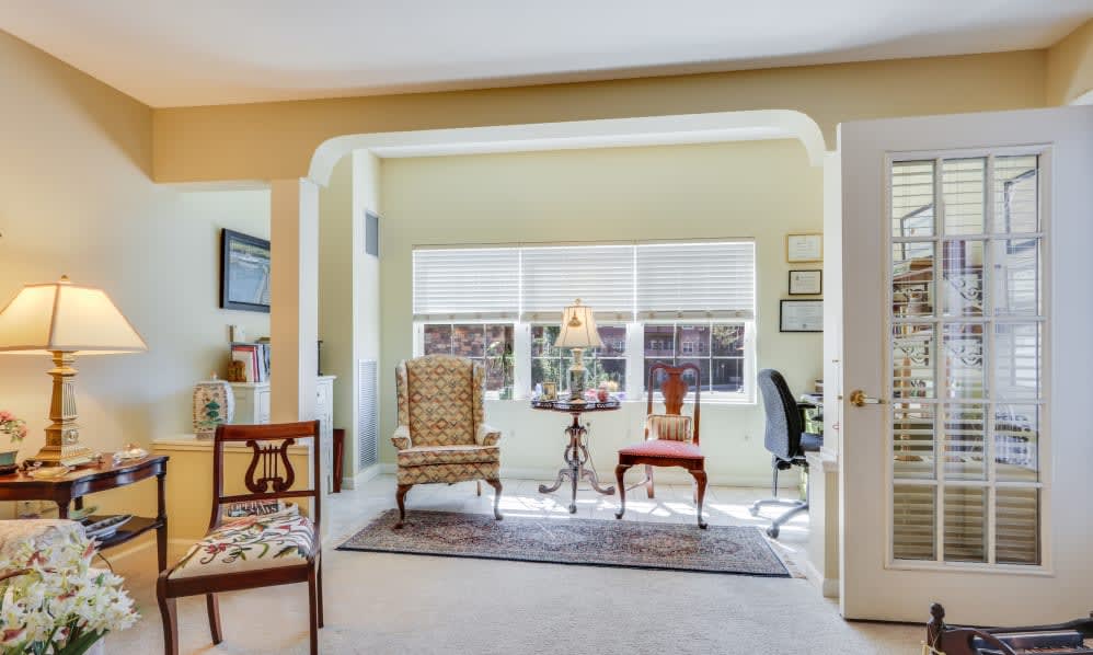 A cozy living room with elegant furniture, featuring two armchairs and a small table near a large window.