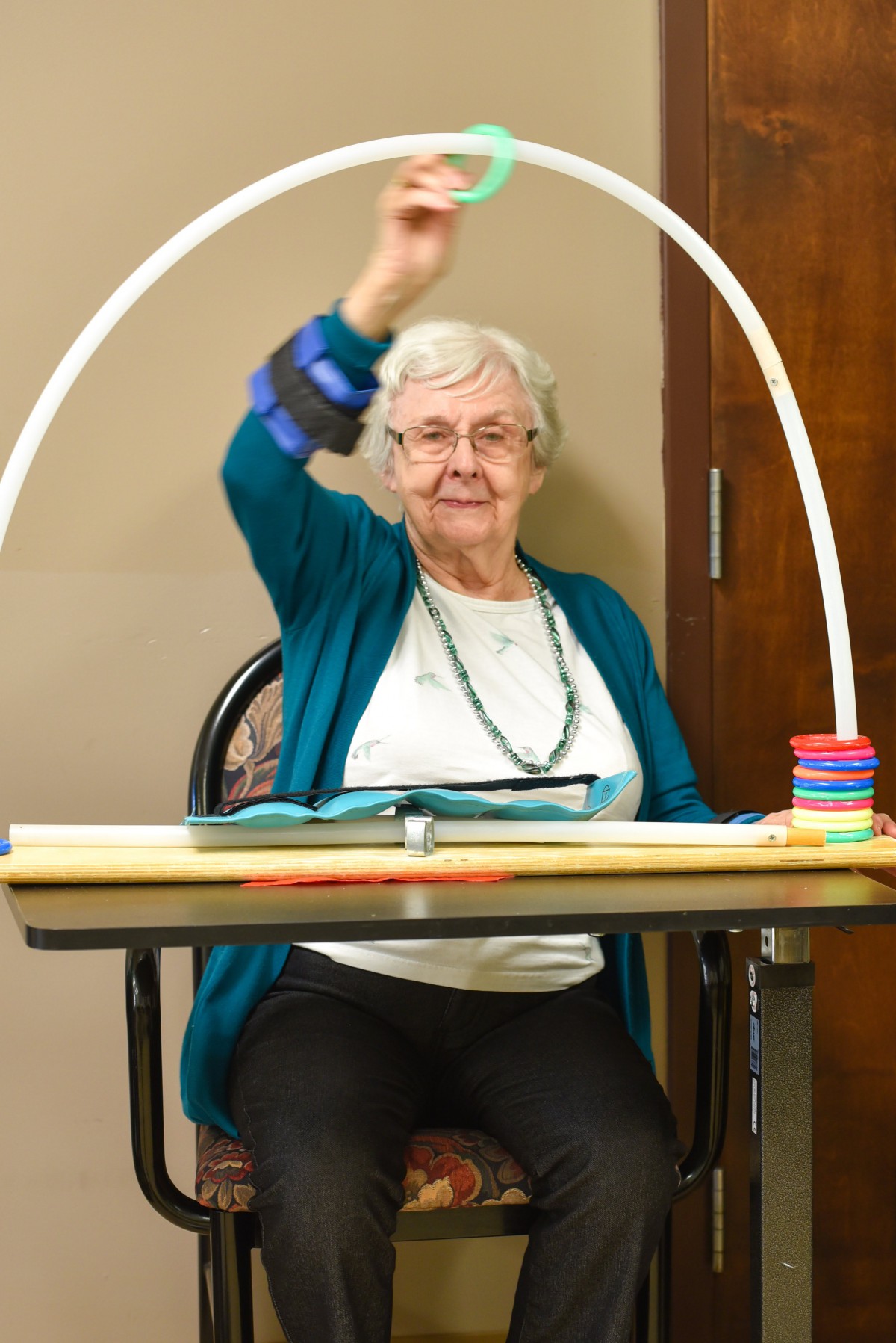 An elderly woman participates in a seated exercise activity using a hula hoop.
