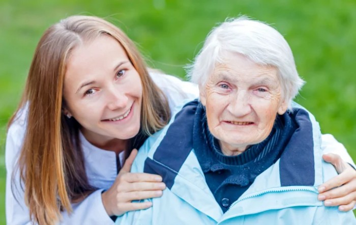 A young woman and an elderly woman smiling together outdoors.