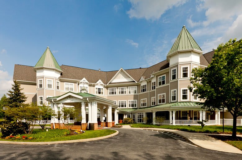 A large residential building with a well-maintained garden and driveway under a partly cloudy sky.