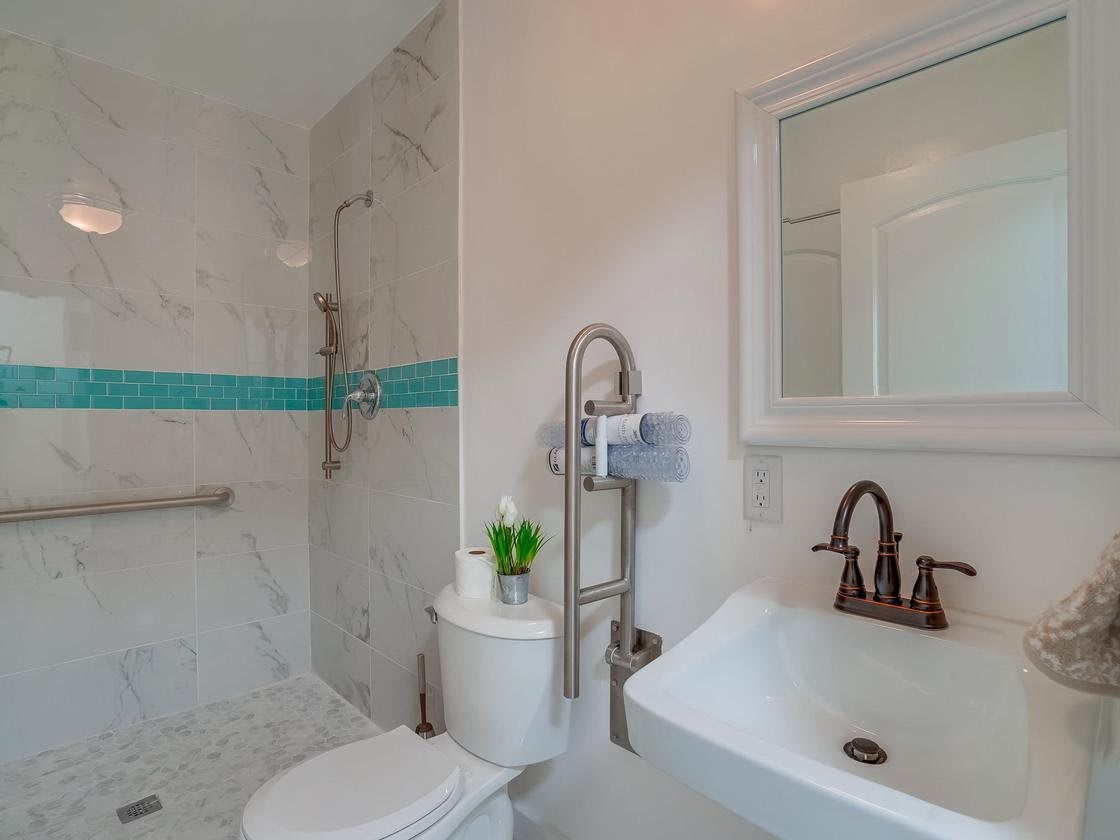 A modern bathroom featuring a shower with white and turquoise tiles, a toilet, and a sink with a mirror above it.