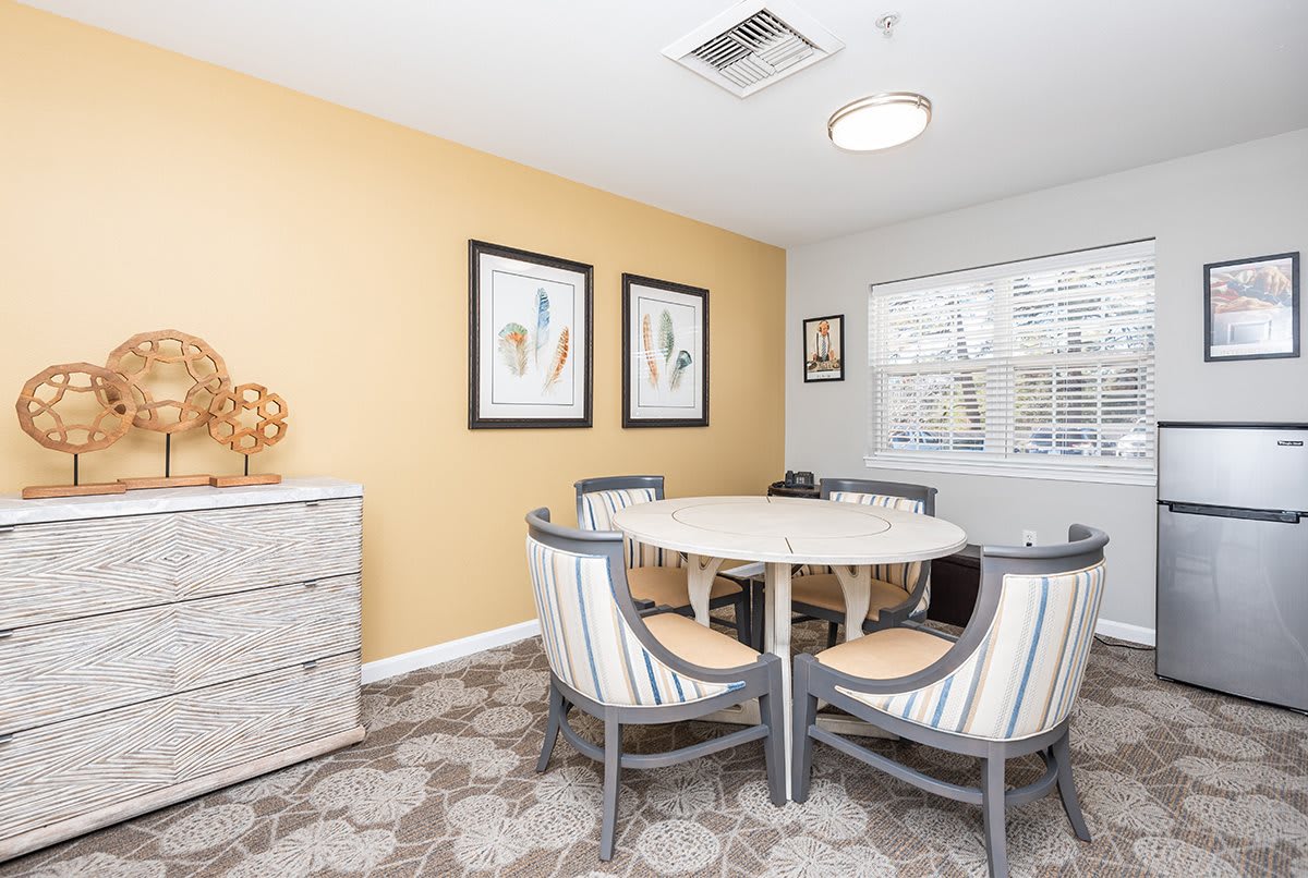 A modern dining room with a round table and stylish chairs, featuring artwork on the walls and a sunny window.