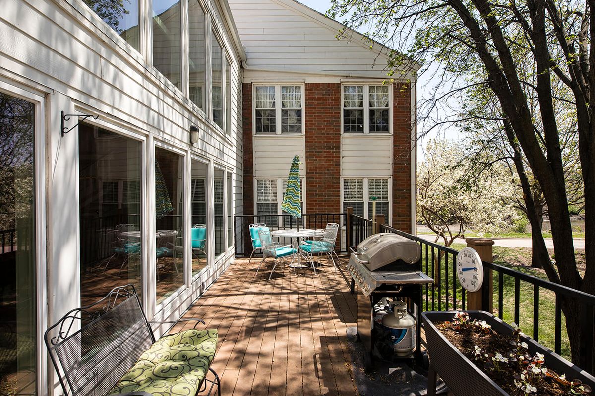 A sunny outdoor patio with a table, chairs, and a grill, surrounded by trees.