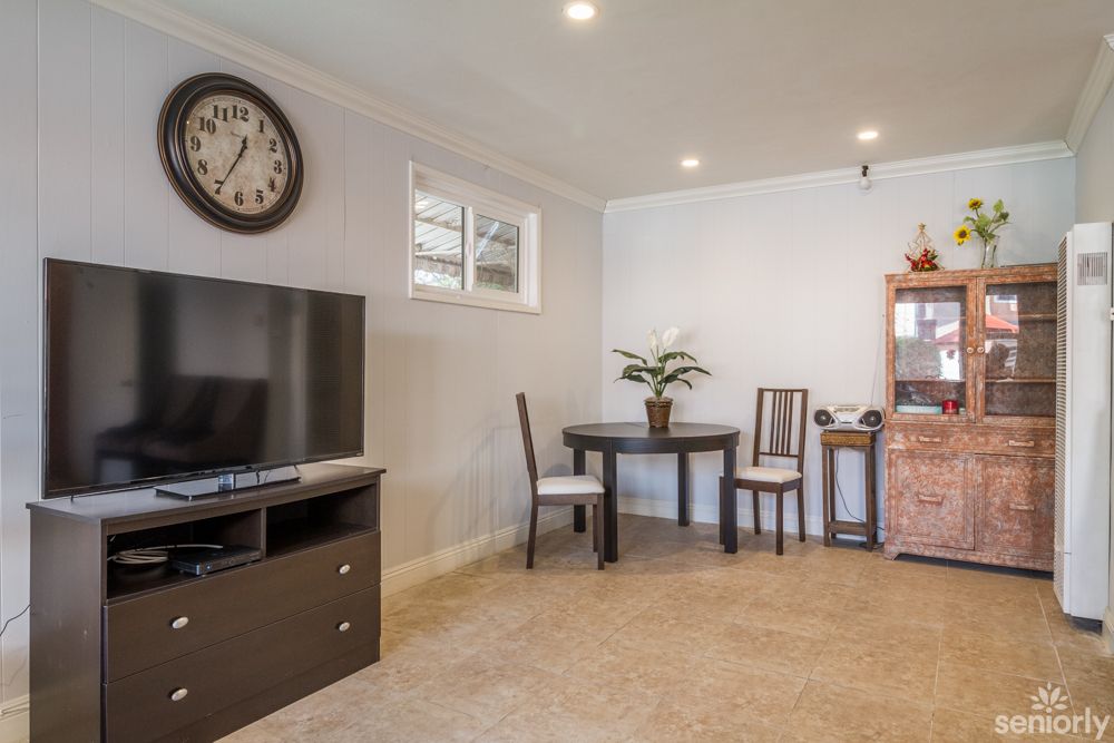 A cozy living room with a television, clock, and a small dining area.