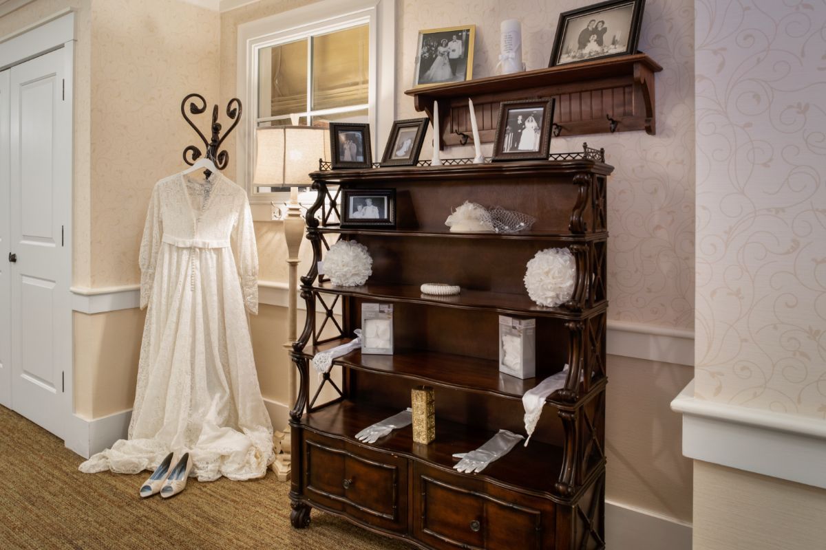 A vintage-themed room with a wedding dress on display next to a shelf adorned with photographs and decorations.