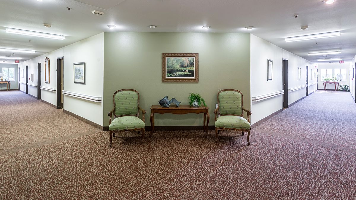 A hallway with two green armchairs and a wooden table between them, adorned with decorative items and a landscape painting on the wall.