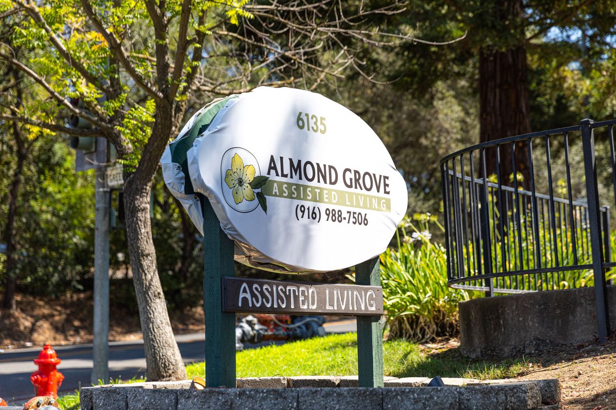 Sign for Almond Grove Assisted Living surrounded by trees.