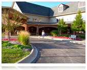 A person walking towards a large building entrance surrounded by landscaped greenery.